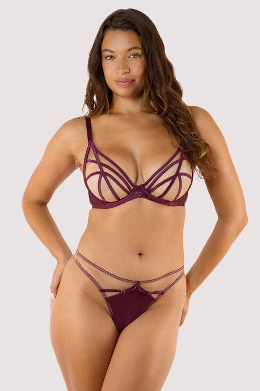 Model wears a wine thong featuring a satin central panel, strap detailing, and gold metal hardware with a matching wine plunge bra.