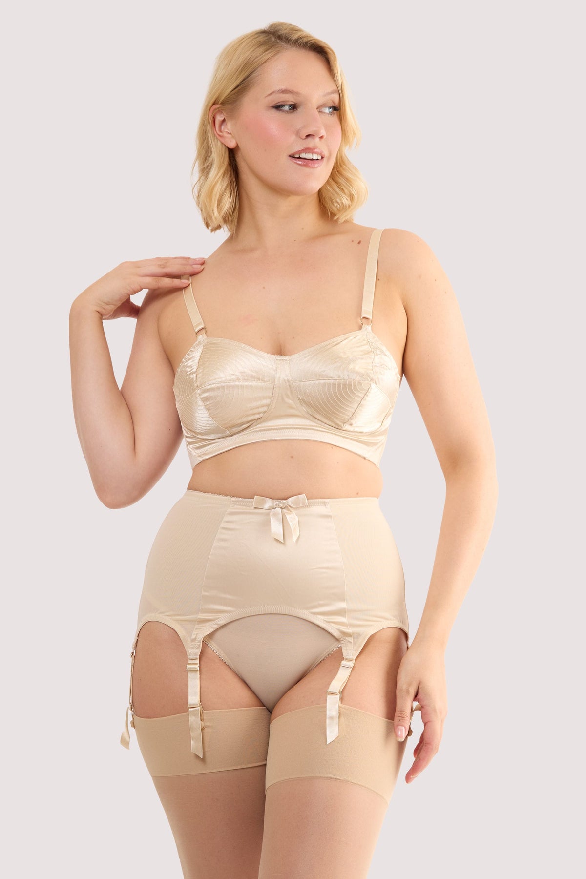 Model wears a champagne satin 6 strap retro everyday suspender with six adjustable straps, soft and smooth finish with a matching brief and bra.