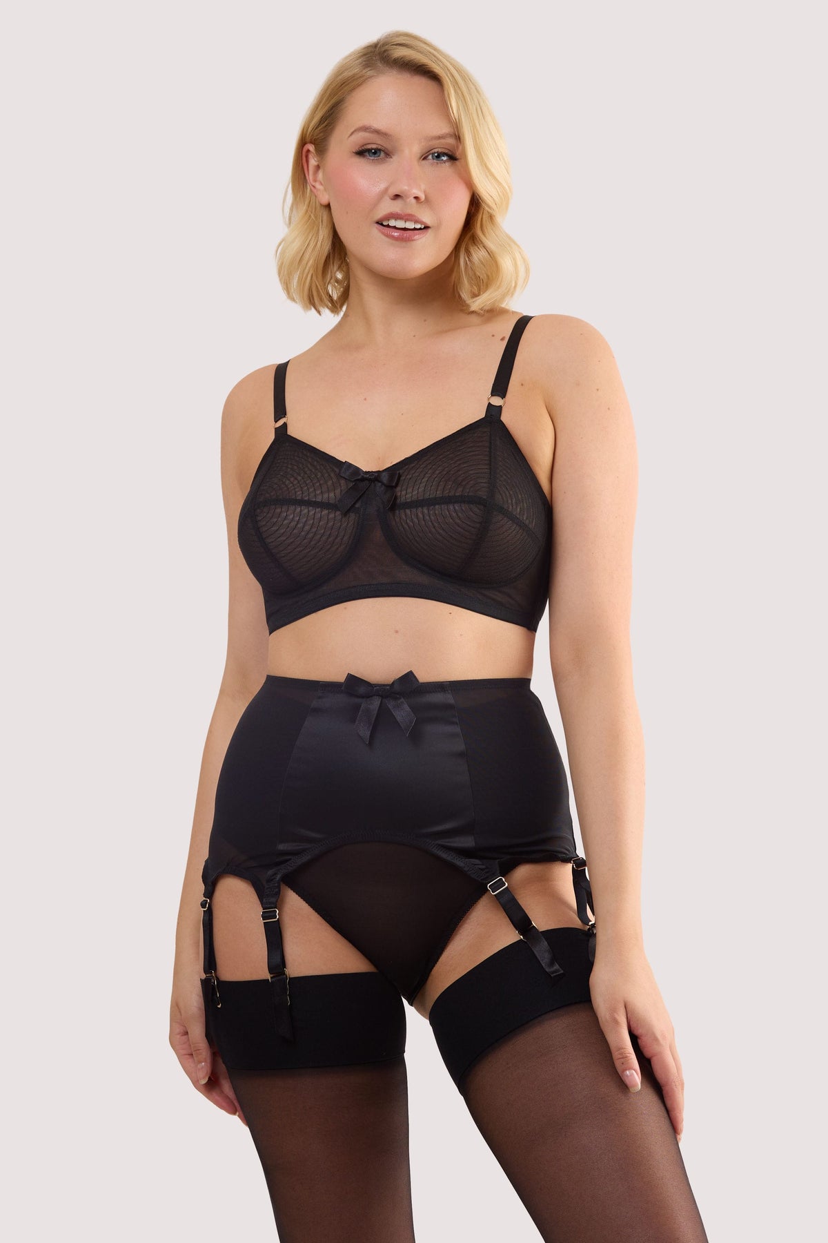 Model wears a champagne black satin 8 Strap retro everyday suspender with six adjustable straps, soft and smooth finish with a matching brief and bra.