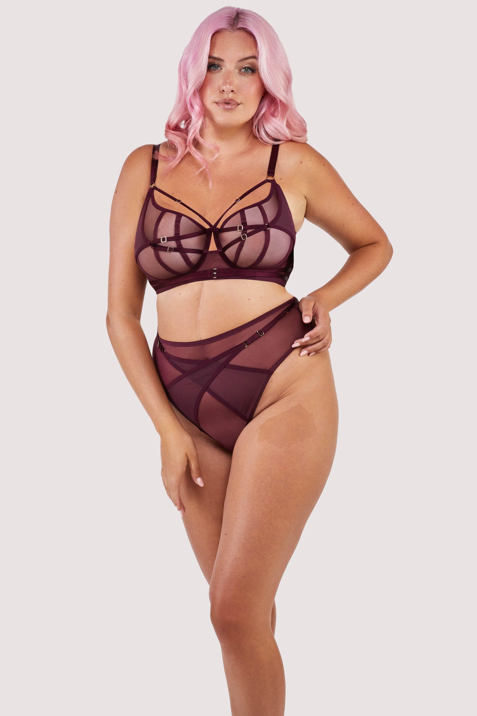 Harness style bra with mesh overlay and visible gold hardware in a deep wine red/purple, worn with a matching brief.