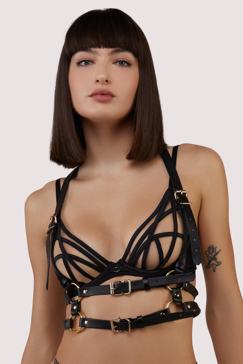 model wears a black bra and black chest harness with buckles