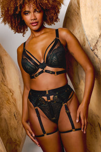 Model wears dark green wet-look lace lingerie set featuring a plunge bra with harness straps high waist brief and suspenders